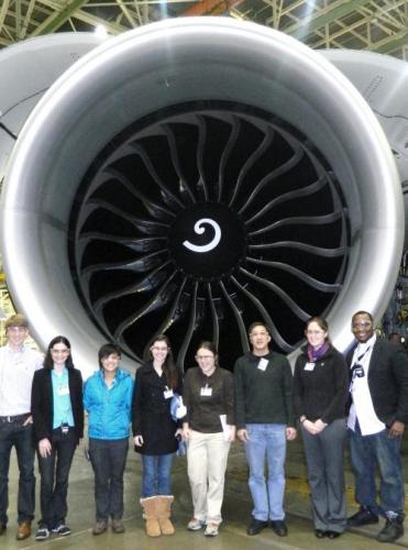 Team members standing in front of a boeing engine