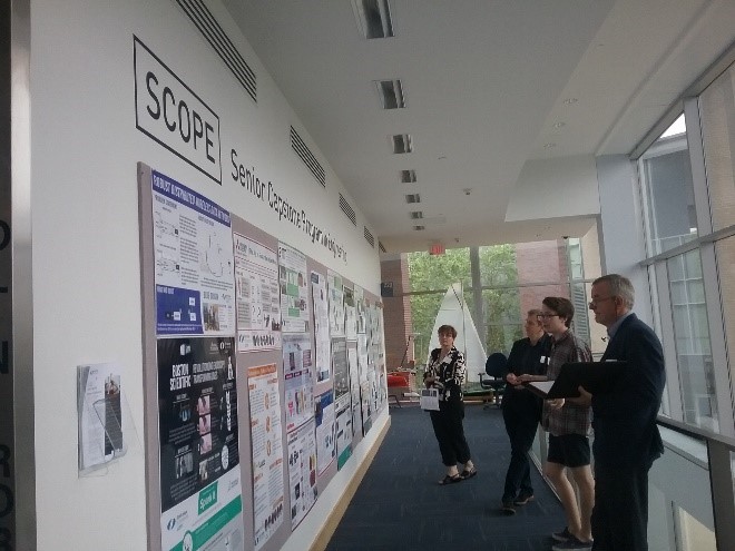 A group of people in a hallway looking at a wall covered with posters about student projects.
