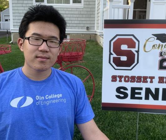 The author wearing an Olin t-shirt standing outside in front of a house and a lawn sign.