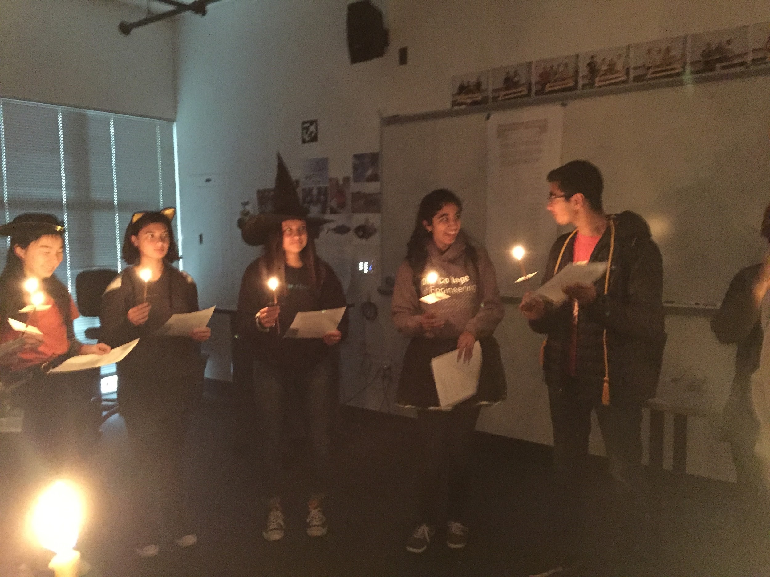 Students wearing costumes and holding lights in a dark classroom.