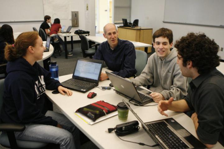 A photo of a group of people in a classroom sitting at a table with laptops
