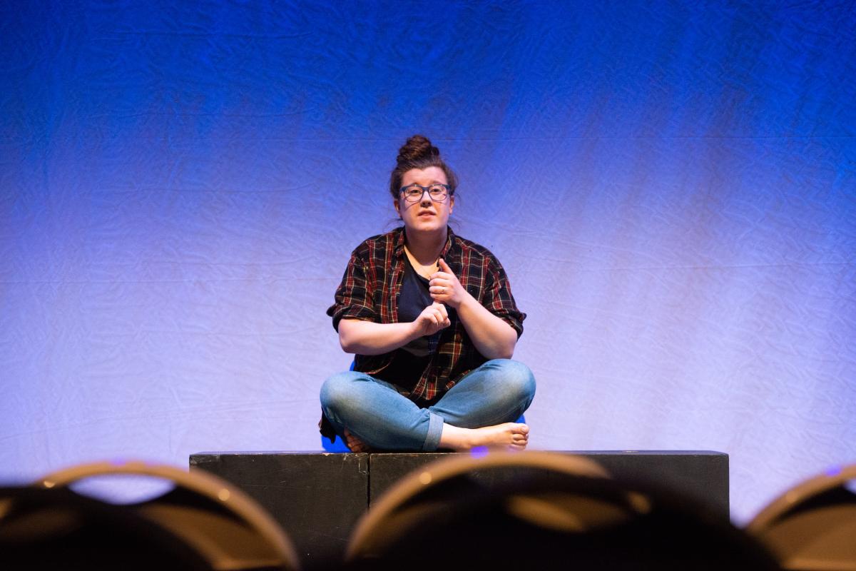 A photo of a person sitting cross-legged on a stage