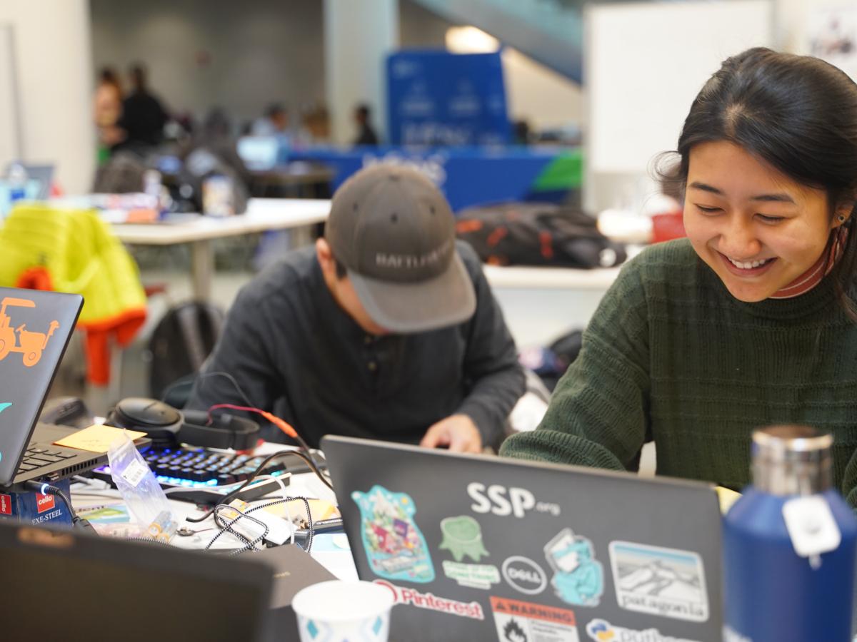Photo of two students working behind a sticker-covered laptop.