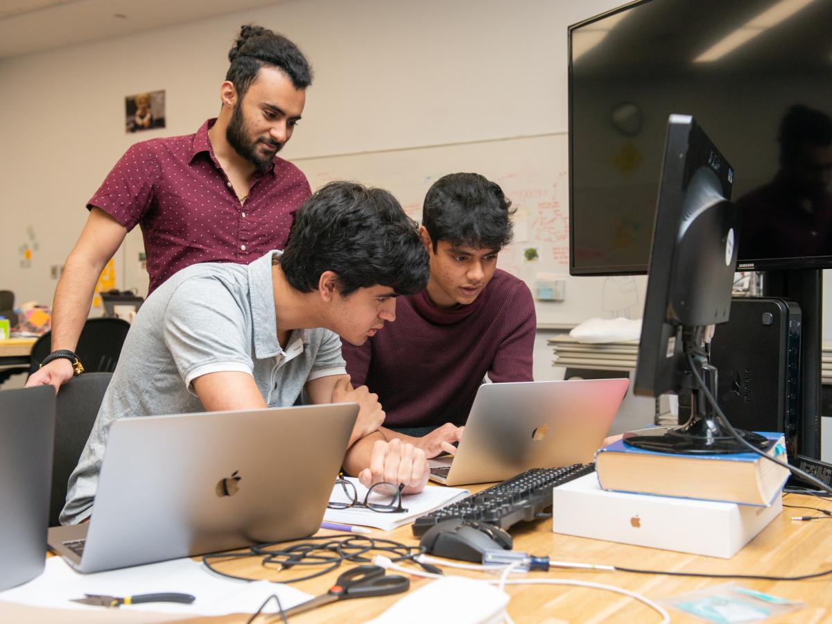 Three Olin student summer researchers hunch over laptops while working in the classroom.