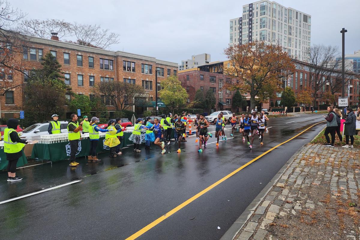 BAA Half Marathon runners race down a rain-slicked street in Boston.
