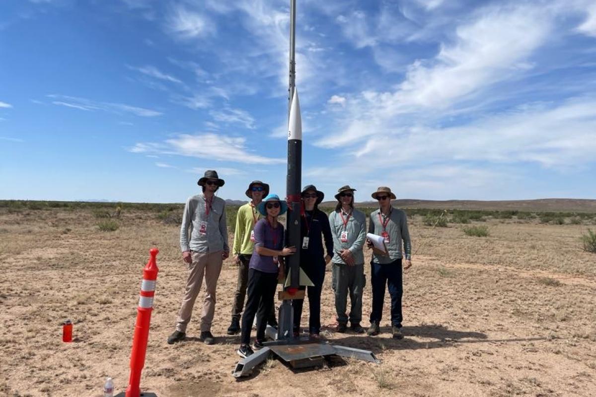 Six people stand in front of a medium-sized rocket.