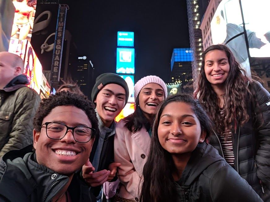 A selfie of a group of friends in Times Square in New York City at night.