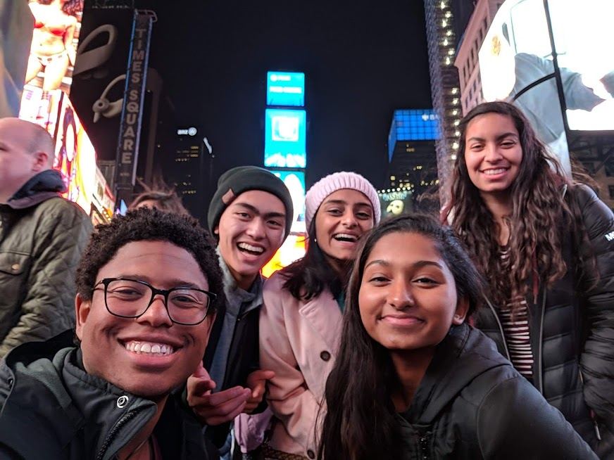 A selfie of a group of friends in Times Square in New York City at night.
