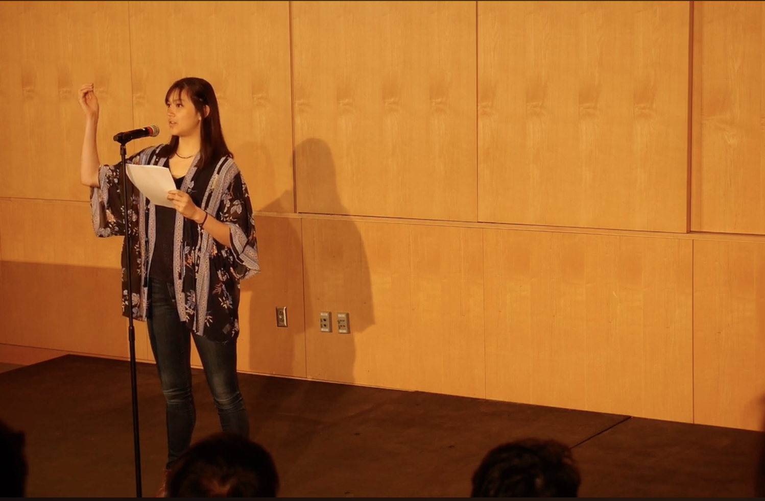 A young woman standing in front of a microphone with her arm in the air