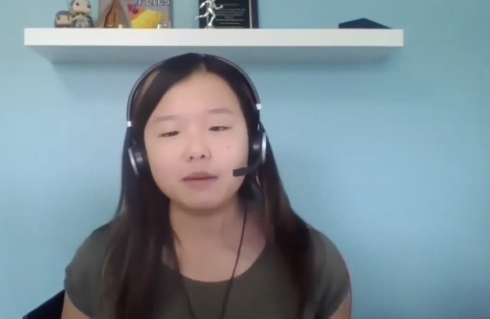 A woman in a room with a blue background wearing a headset on a zoom call