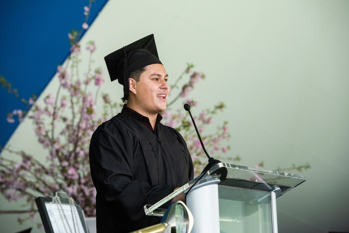 A young man standing at a podium wearing a cap at gown