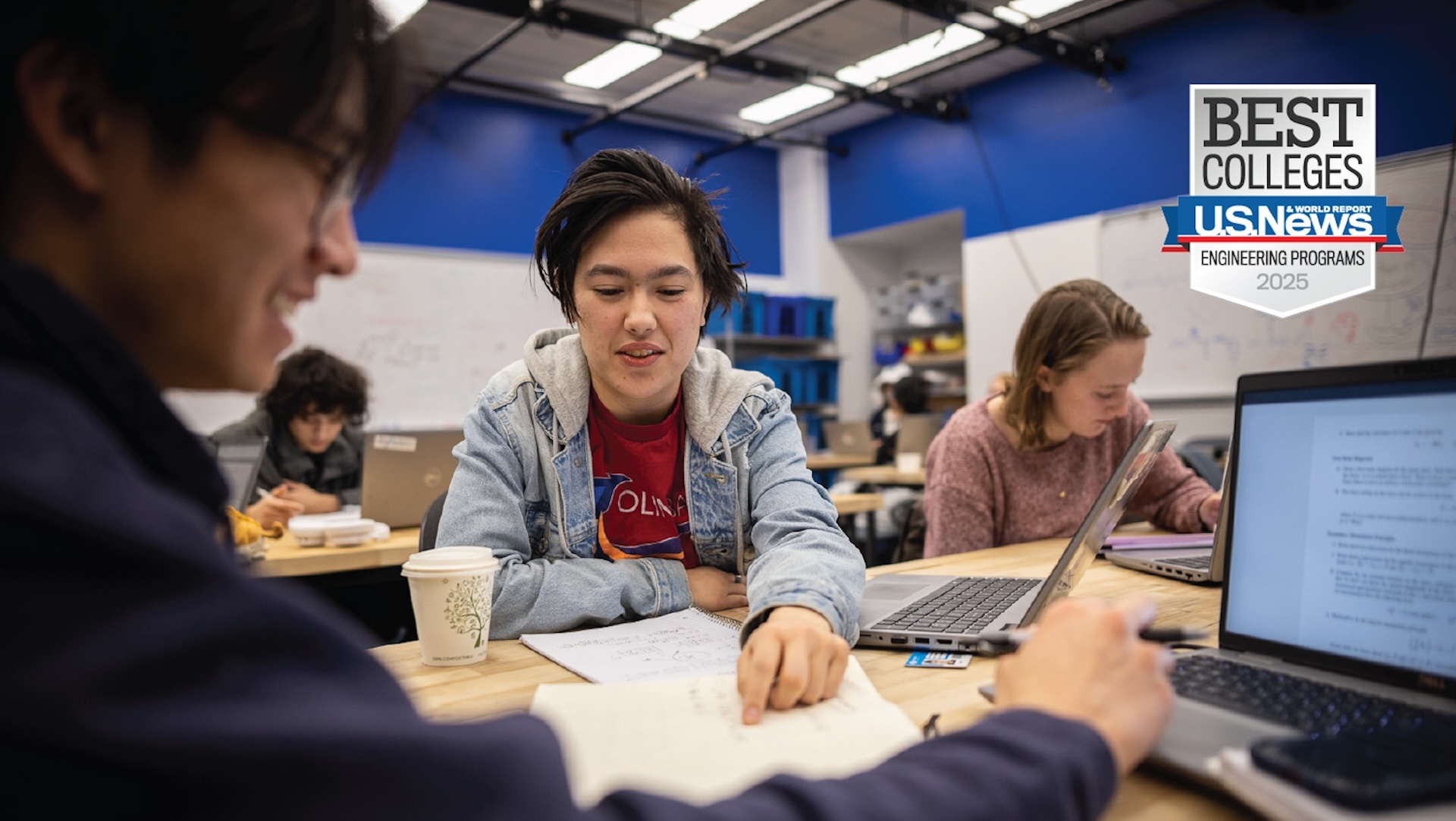 An Olin engineering student works with classmates in a classroom.
