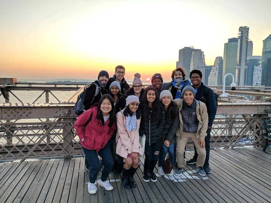 A group of friends on a bridge with a sunset and city skyline in the background.