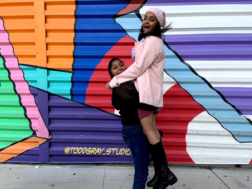 Two friends embracing in front of a colorful mural.