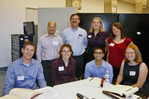 Team members sitting and standing around a desk smiling