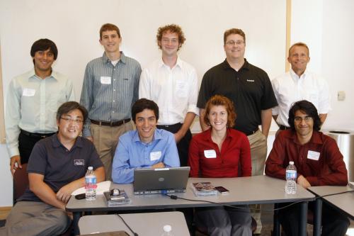 Team members sitting and standing around a desk smiling