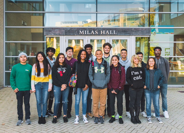 A group of students standing outside in front of a building labeled "Milas Hall."