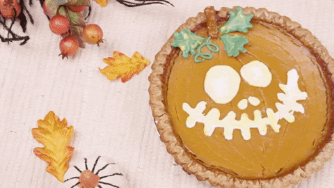 Halloween-themed pumpkin pies on a table decorated with leaves and spiders.