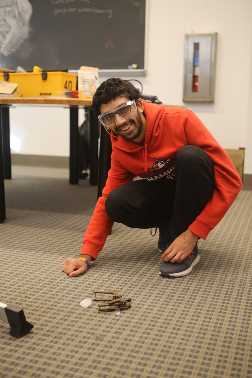 A student wearing safety glasses crouching on the floor with an engineering project.