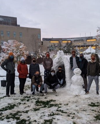 A group of students outside in the snow next to a snowman and igloo.