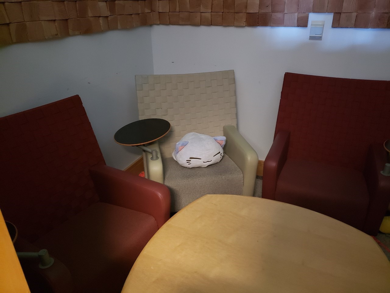 Three chairs, a table, and a cat-shaped pillow in a corner.