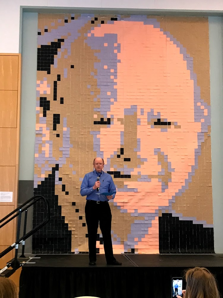 Olin's former president Rick Miller standing in front of a sticky note mural of his face.