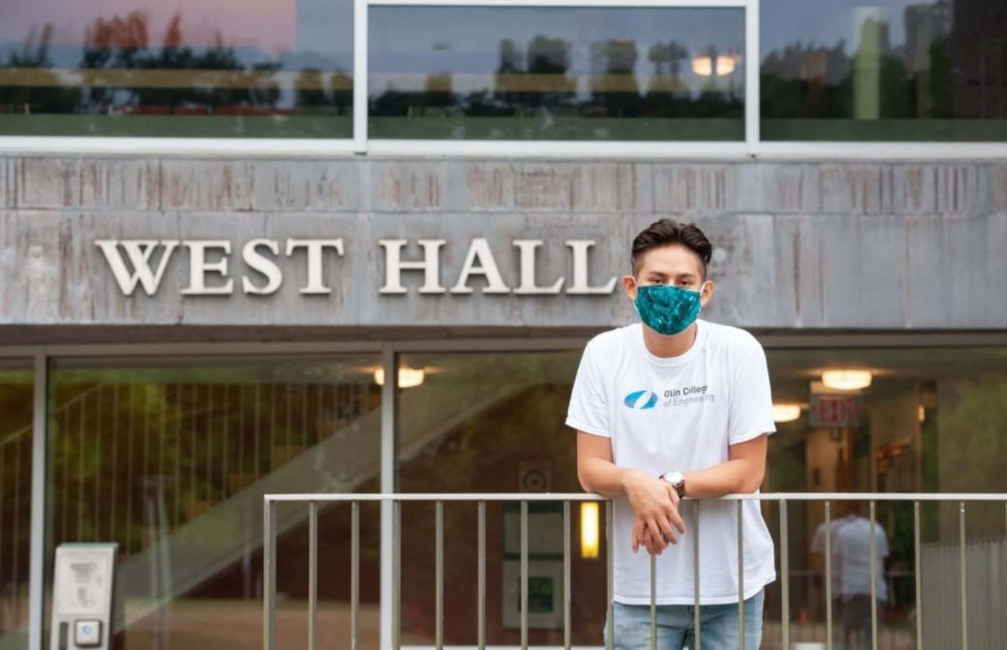 The author standing outside Olin's West Hall residence hall, wearing an Olin t-shirt and a mask.