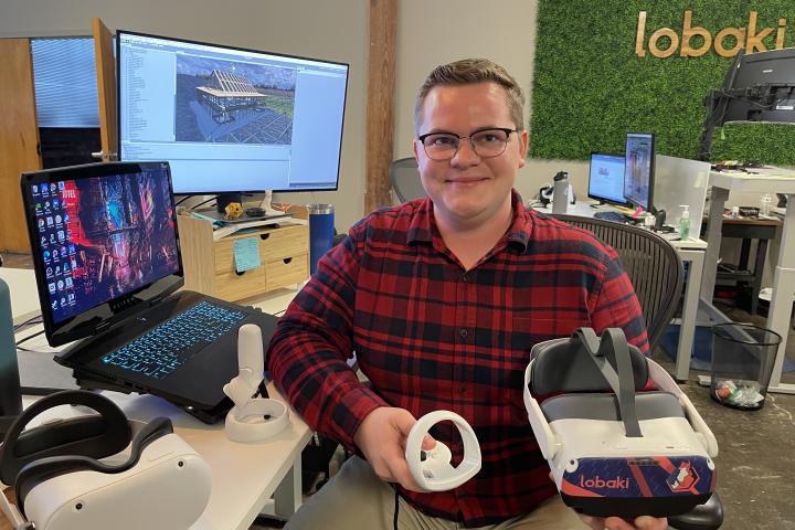 A photo of a man wearing a red and black shirt holding a virtual reality headset. 