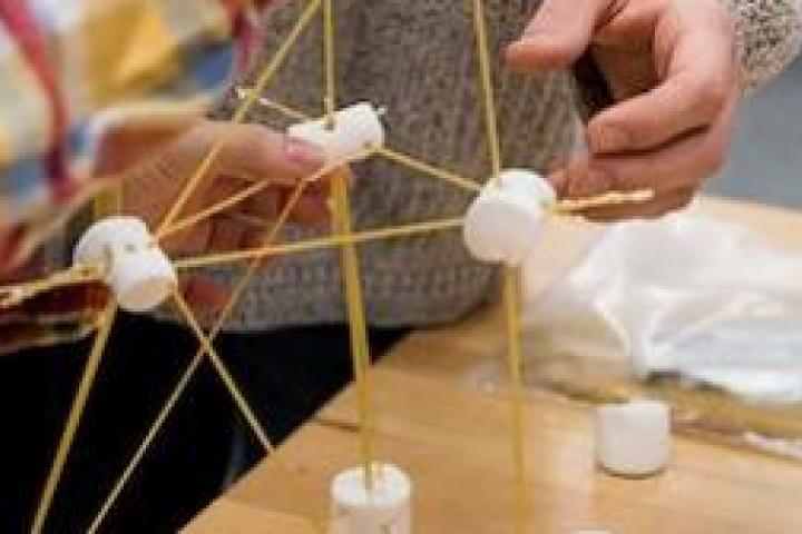 Closeup of people building a structure out of marshmallows and spaghetti