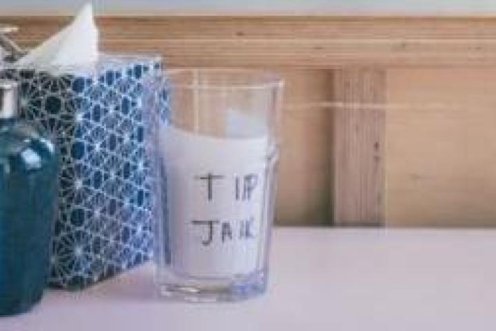 A soap dispenser, tissue box, and tip jar on a table.