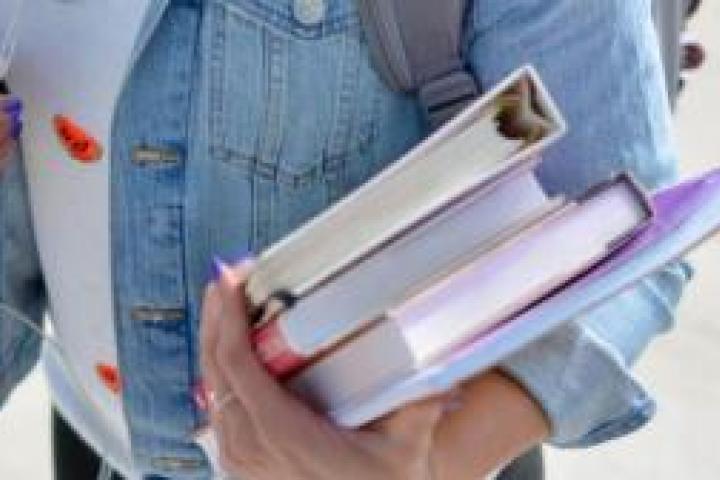 A closeup of a person wearing a backpack and headphones and holding schoolbooks.