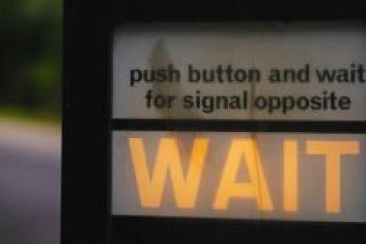 Closeup of a stoplight that says "push button and wait for signal opposite; WAIT"
