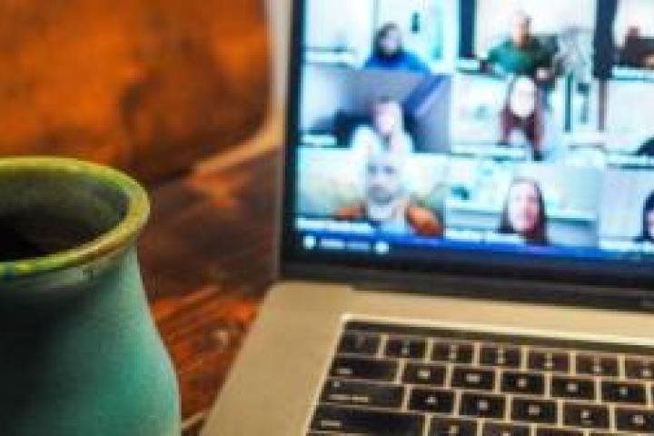 A laptop displaying a zoom call next to a coffee mug.