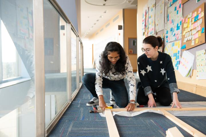 Olin students working together on a Buildweek 2020 project. Two students working together on a project that is laid out on the floor.