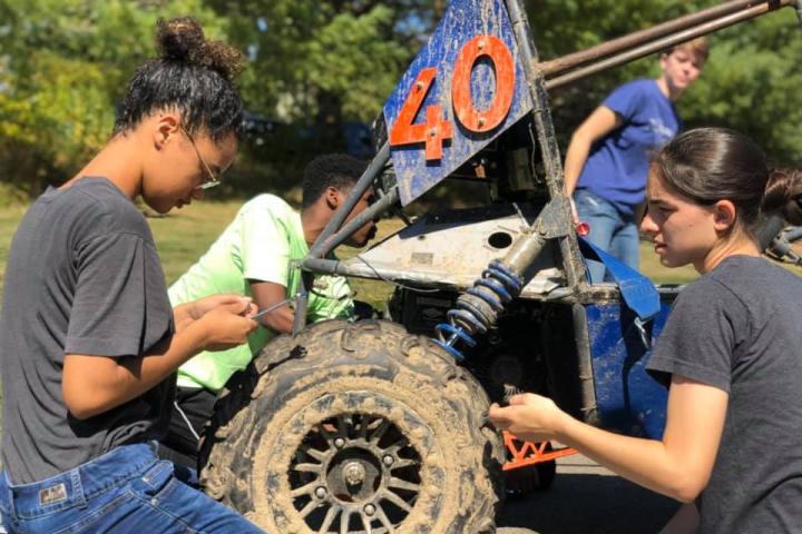 A group of engineering students encircle their their off road baja vehicle