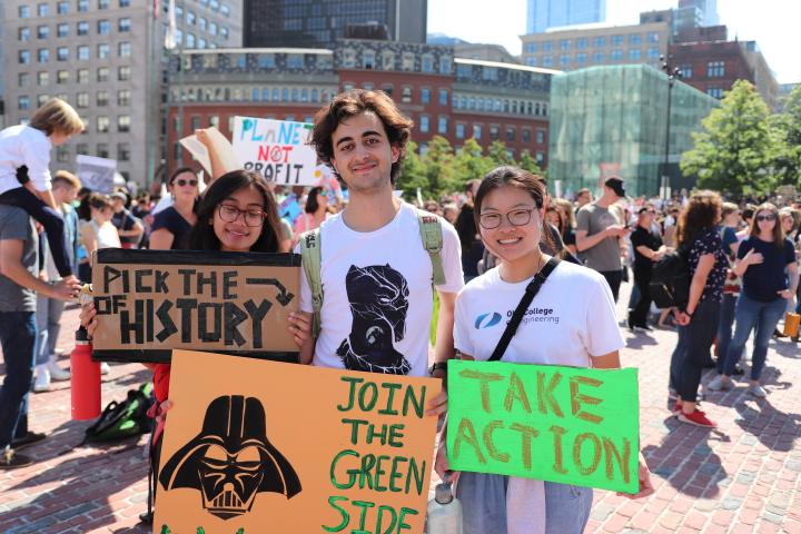 A photo of three college students standing next to one another holding signs at the Boston Climate Strike