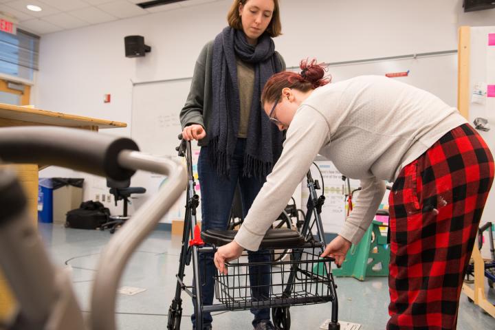 A photo of two young women in a classroom working to modify a walker