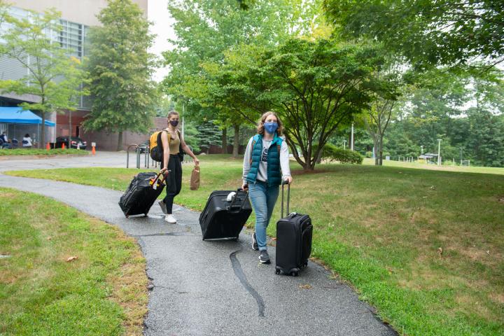 A photo of two people wheeling suitcases down a path