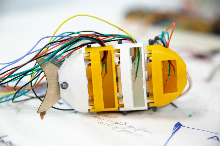 A photo of a white and yellow plastic robotic fish prototype with wires protrding from its back