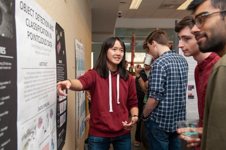 An Olin student shares her research poster with other students A photo of a student pointing to a poster on the wall