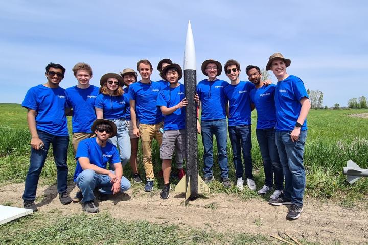 Members of the Olin College Rocketry Team in blue shirts pose in front of one of their rockets.