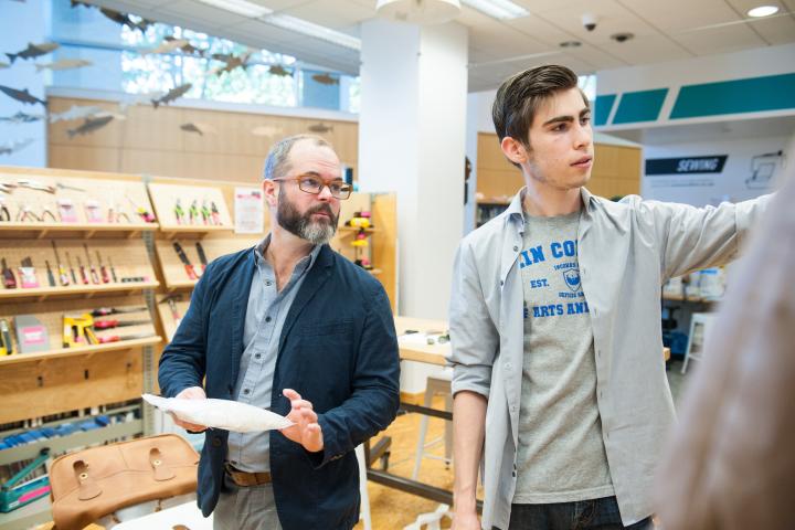 Two people in a library look at something on a wall off camera.