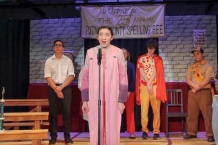 Olin College Admission Ambassador Cara Mulrooney A photo of a person standing on a stage talking into a microphone