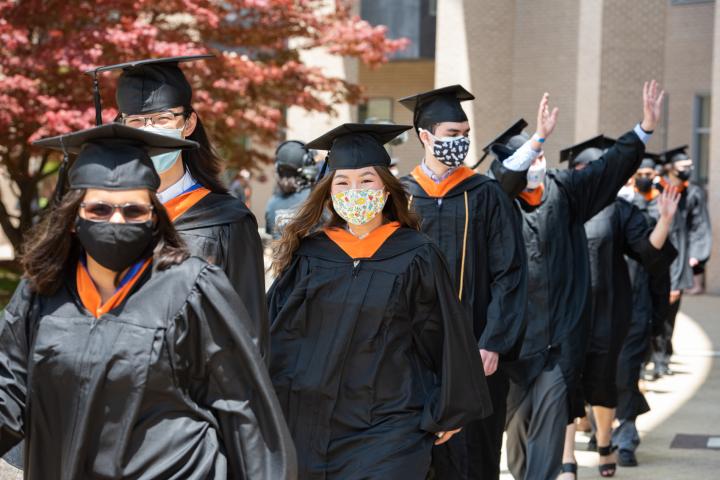 A line of students in cap and gown wave and process down to the Olin Commencement Tent.