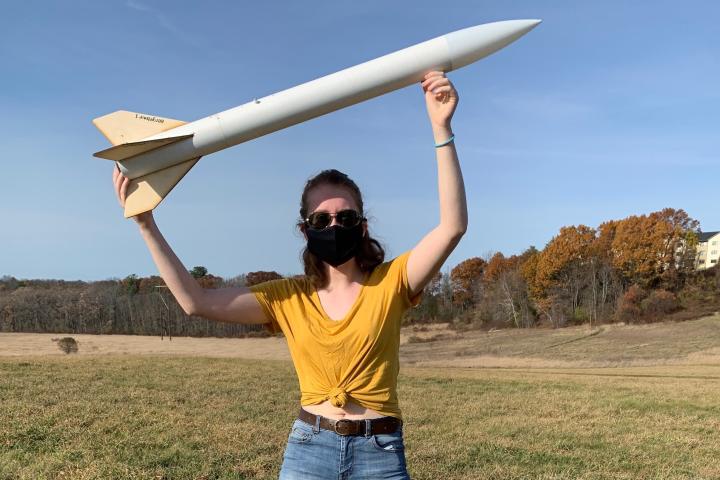Olin College Admission Ambassador Esme Abbot A photo of a young woman in a field holding an autonomous rocket