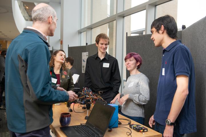 Three students behind a table present their hexapod to another person at Fall Expo 2019