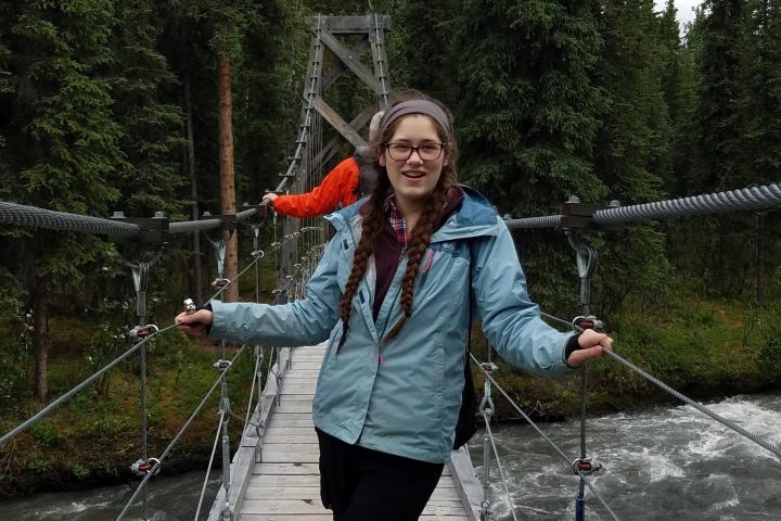 A photo of a young woman standing on a rope bridge