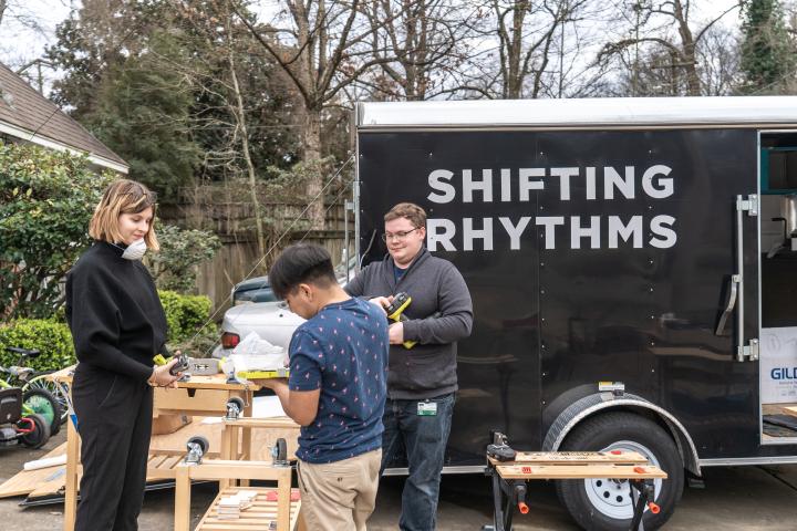A photo of three students working outside at a workbench with a trailer in the background