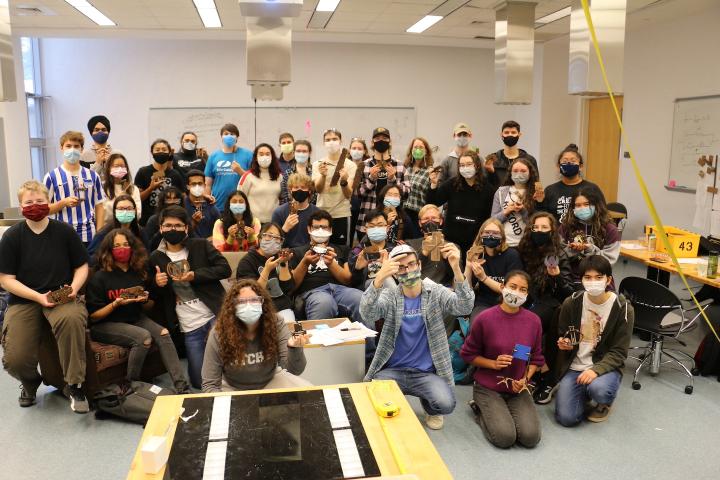 A group of students with face masks on pose for a group photo in a classroom