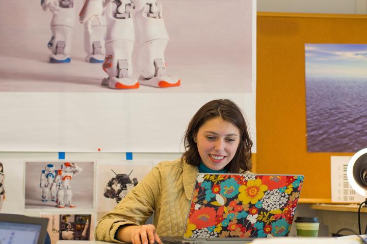A student with an open, flower-graphic laptop works at a table and smiles.